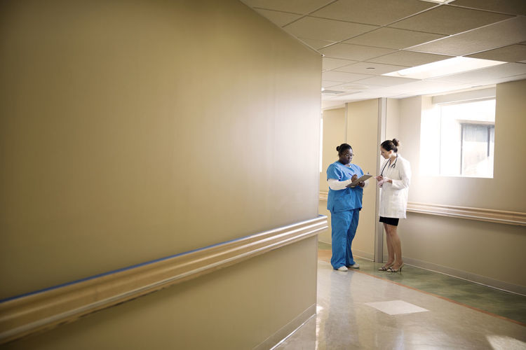 Doctor and nurse with clipboard discussing while standing in corridor