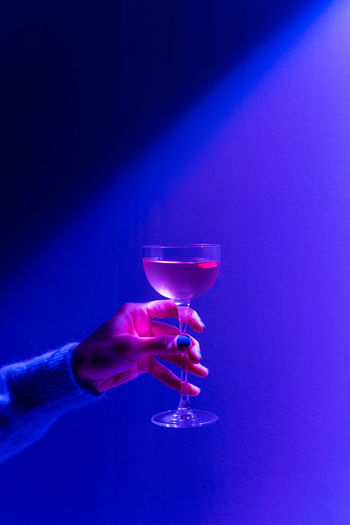 Hand holding elegant glass with an alcoholic cocktail. alcoholic drink in neon lights