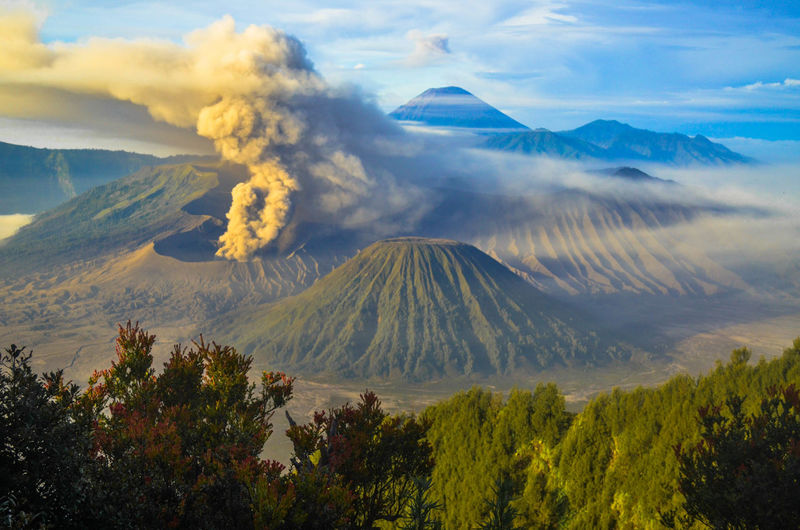 Scenic view of volcanic mountains erupting ashes against sky