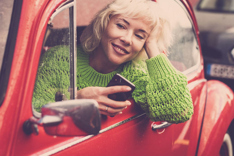 Smiling woman using mobile phone while sitting in car