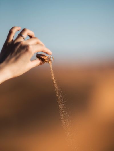 Close-up of woman hand pouring sand from bottle in desert