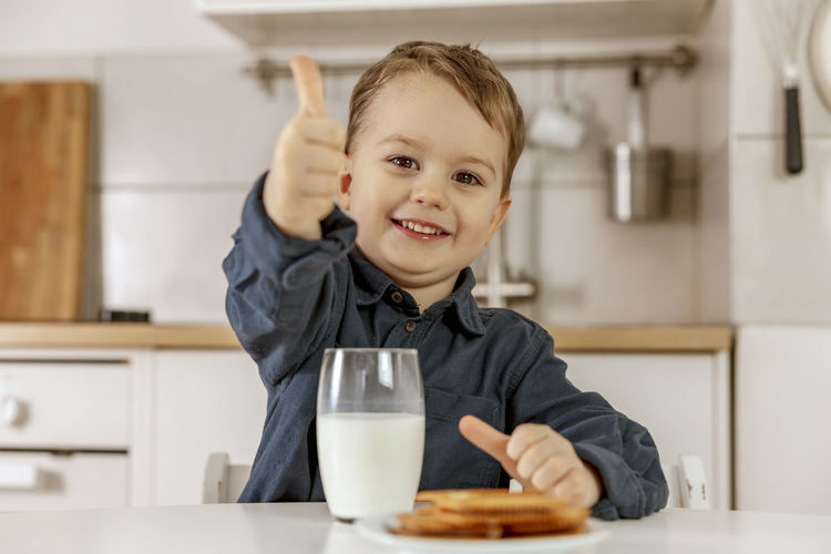 Little boy sitting in the kitchen and drinking milk. fresh milk in glass, dairy healthy drink. 