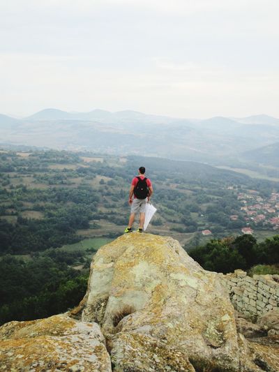 Rear view of man standing on cliff against sky