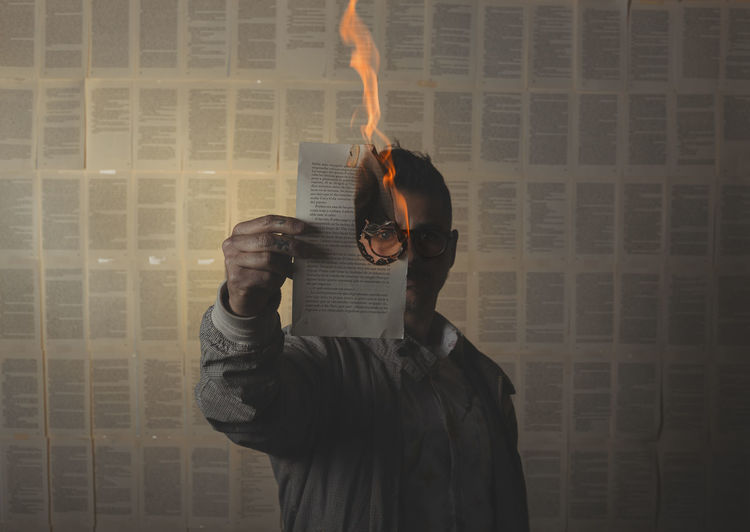 Man holding a burning book sheet and looking through it. conceptual image.
