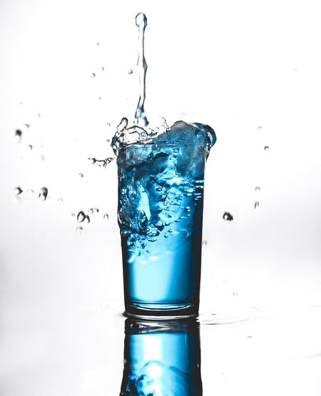Close-up of water splashing on glass against white background