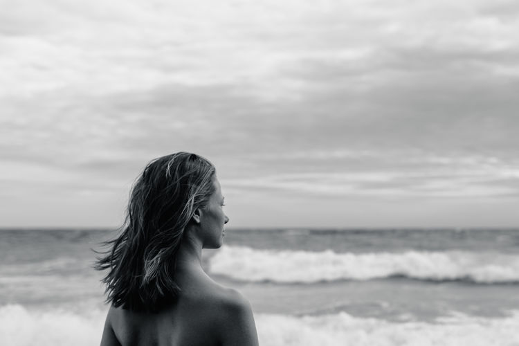 Rear view of young woman standing at beach against sky