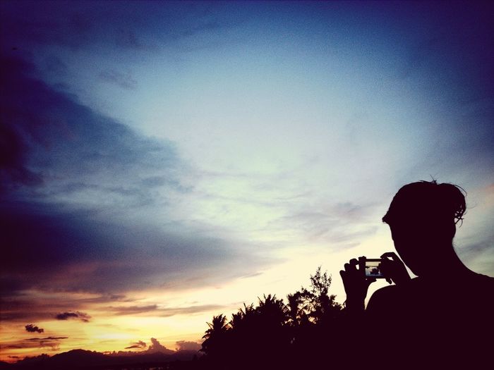 Silhouette person photographing landscape at sunset