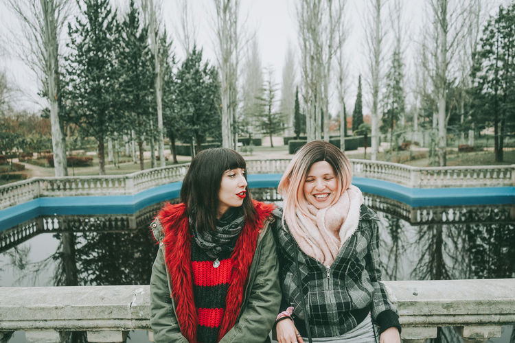Smiling friends leaning on railing against lake during winter