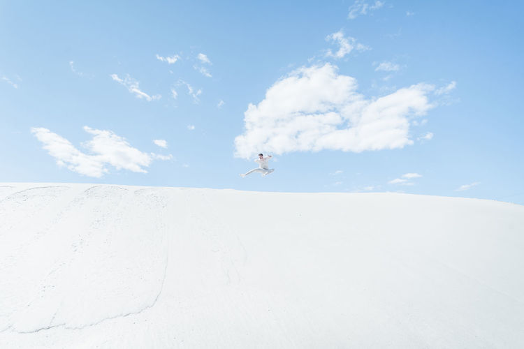 Man jumping on desert against sky