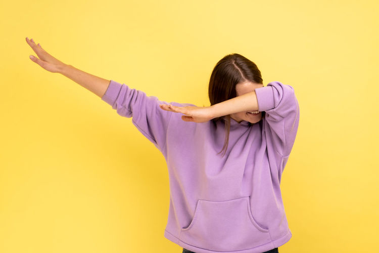 Young woman with arms raised standing against yellow background