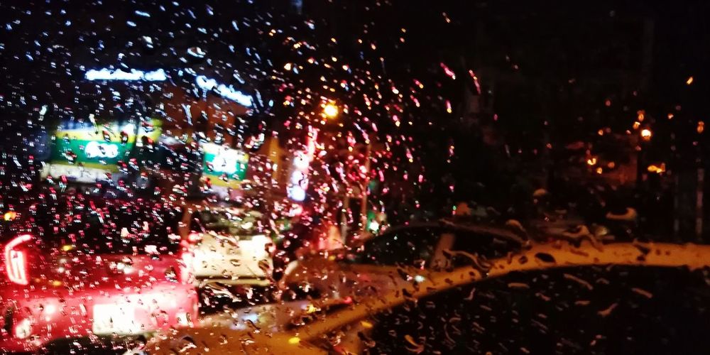 Illuminated city seen through wet window during rainy season
