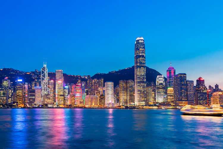 Illuminated buildings in city against blue sky