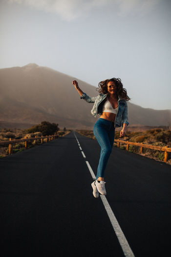 Portrait of happy young woman on road against sky