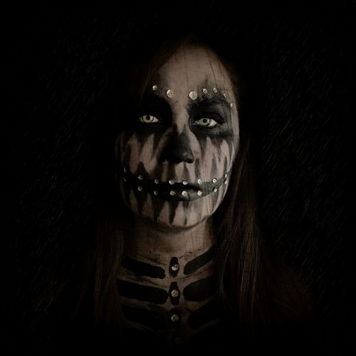 Portrait of woman with skull face paint against black background