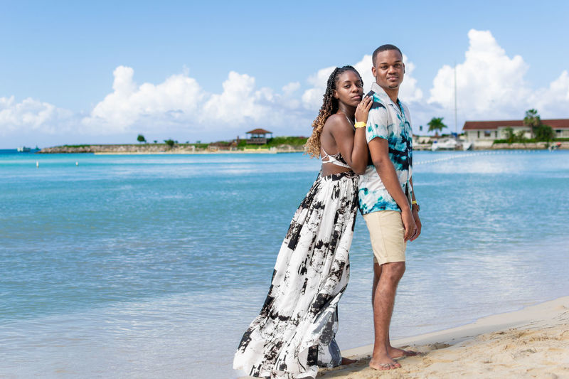 Portrait of a young  couple standing on the beach against the sea and clear sky