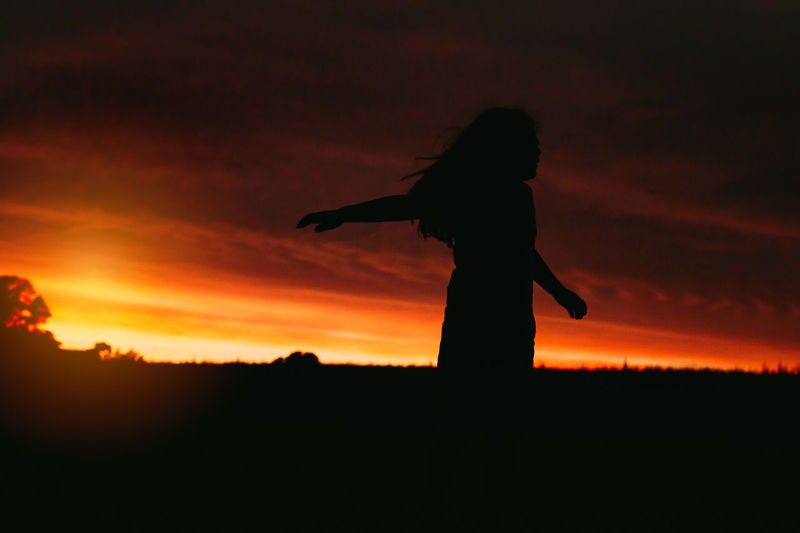 Silhouette woman standing on field against orange sky