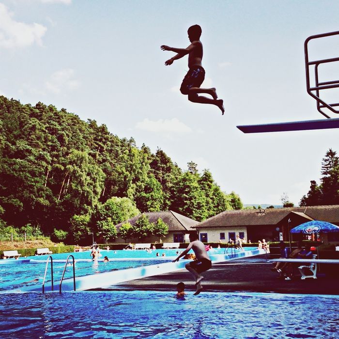 Man jumping into swimming pool against sky
