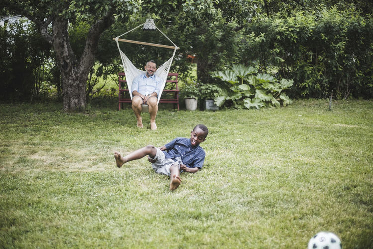 Man swinging while looking at boy playing in backyard