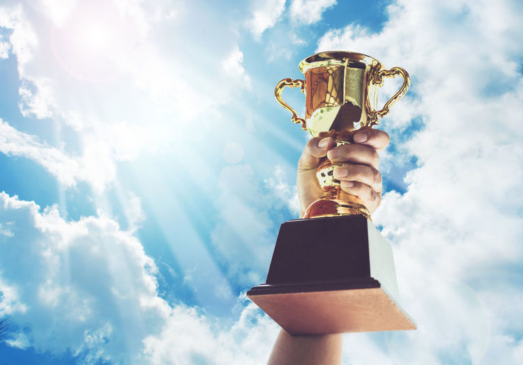 Cropped hand holding trophy against cloudy sky