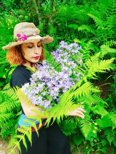Beautiful young woman wearing hat standing against plants