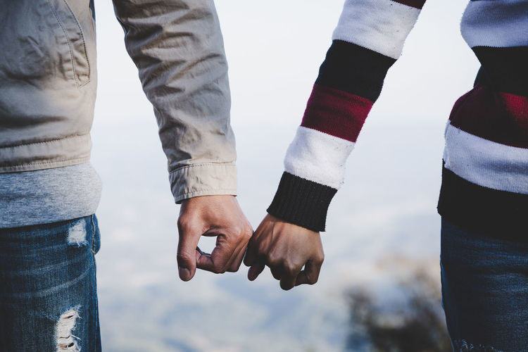 Midsection of couple taking pinky promise outdoors