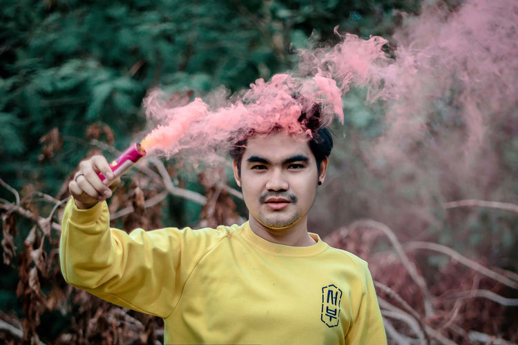 Portrait of young man holding distress flare against tree