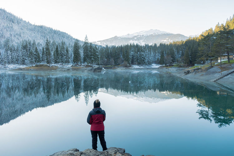 Rear view of woman standing by lake against clear sky