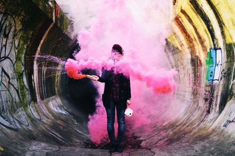 Man holding smoke bomb and camera while standing in tunnel