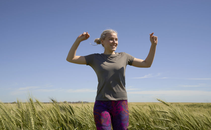Young woman runner raises her arms after running in the field