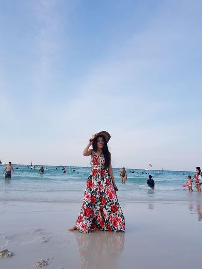 Woman wearing floral patterned dress while standing on shore at beach against sky