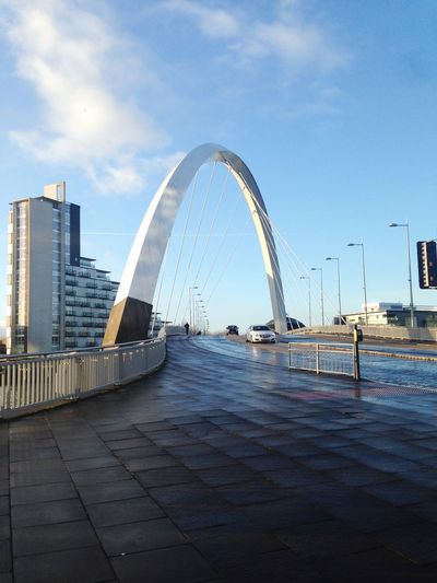 Bridge over river by modern buildings against sky