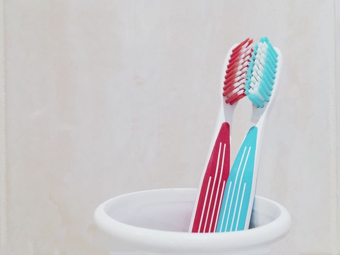 Close-up of toothbrushes in container against white wall