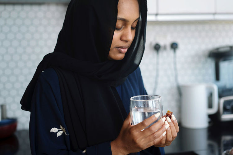 Muslim woman wearing abaya breaking fast during ramadan eating dates drinking water