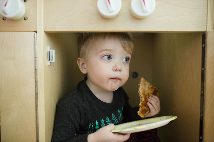 Toddler boy looks off into distance while eating pizza on paper plate