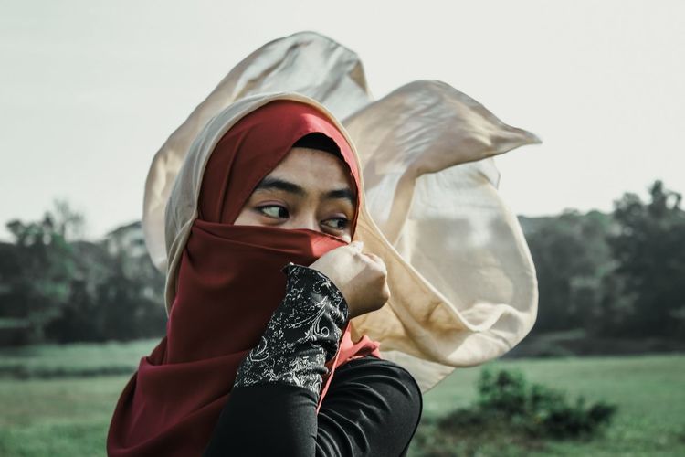 Young woman wearing hijab while standing against trees and sky