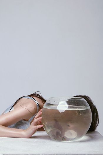 Woman with fish bowl at table against white background
