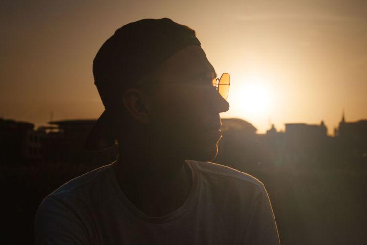 Portrait of young man drinking sunglasses against sky during sunset