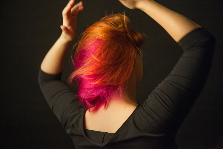 Rear view of woman dancing against black background with colorful hair