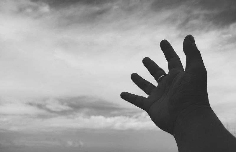 Cropped hand of person against cloudy sky