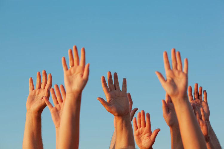Cropped image of people with arms raised against clear sky