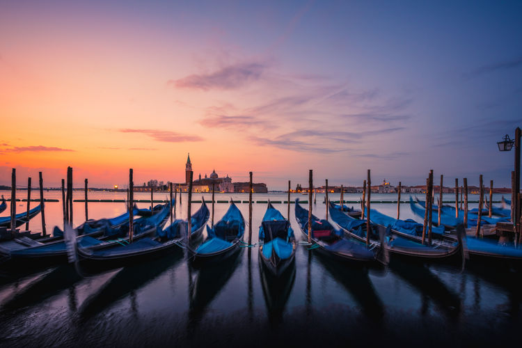 Gondolas moored at harbor during sunset