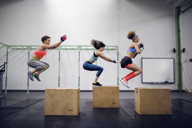 Side view of determined female athletes doing box jumping at health club