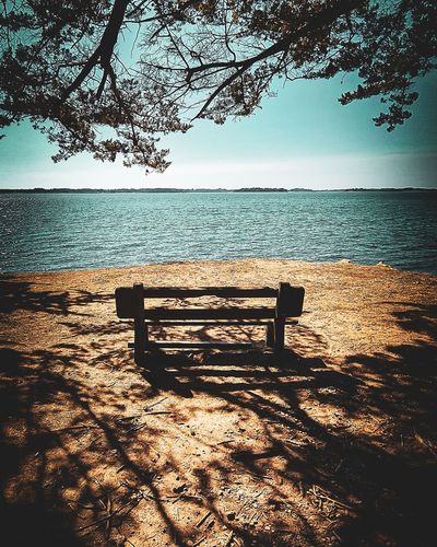Empty bench by sea against sky