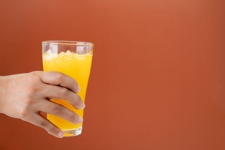Cropped hand holding drink against yellow background