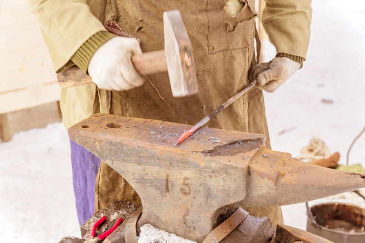 Midsection of blacksmith hammering metal on anvil