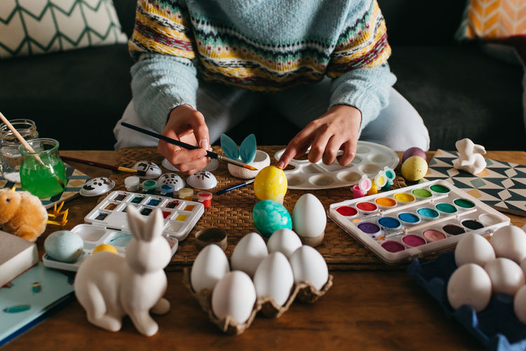 Unrecognizable person in sweater covering fresh chicken eggs with yellow paint while preparing for easter celebration person