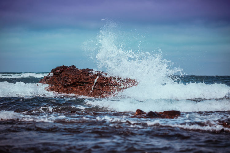 Water splashing on rock in sea against sky