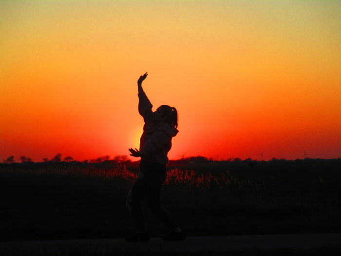 Girl dancing while walking on road against orange sky