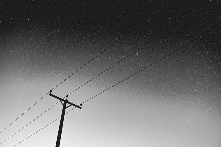 Low angle view of silhouette electricity pylon against sky at night