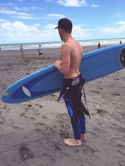 Full length of shirtless man with surfboard at beach